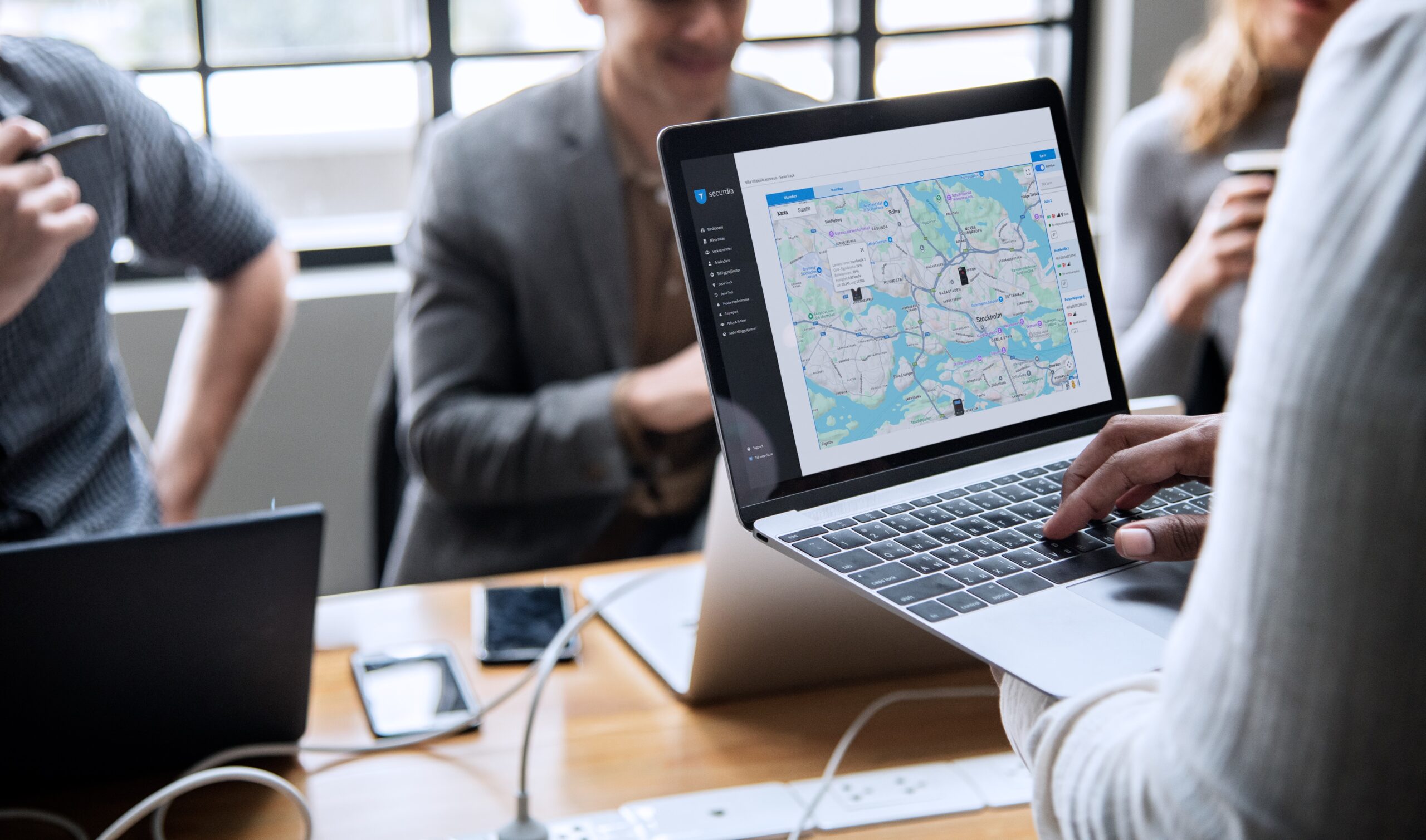 Person håller en laptop med en karta på skärmen under ett möte i ett kontorsrum.